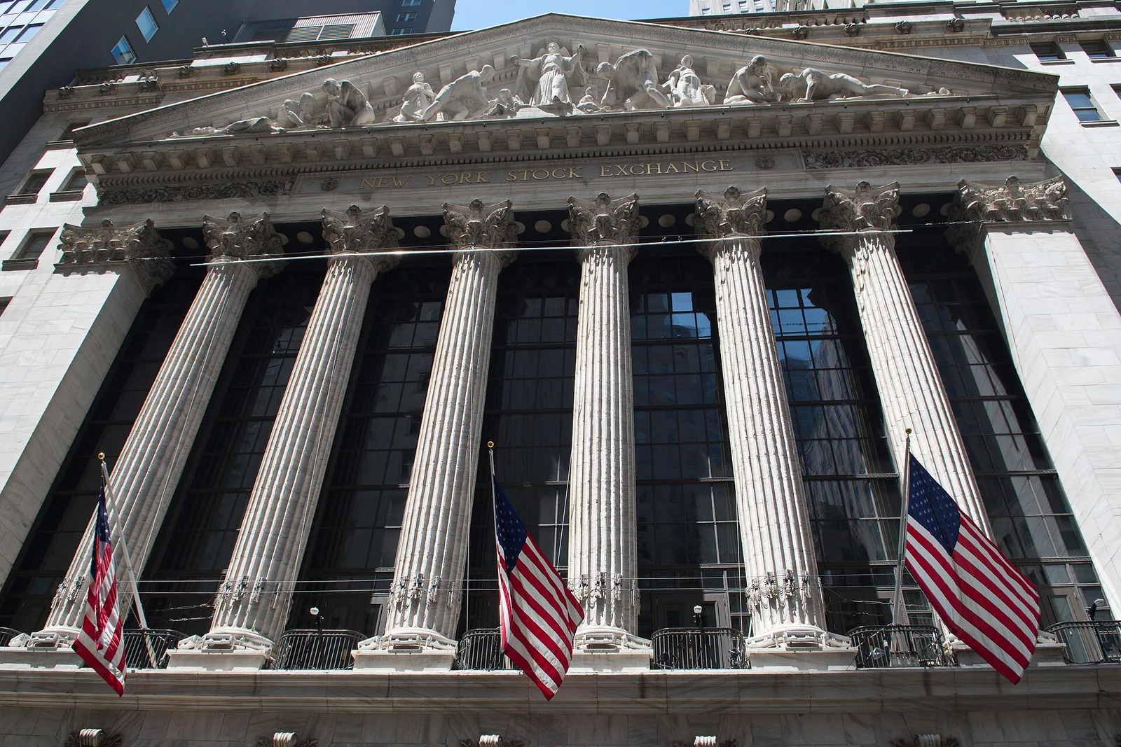 Columned facade of the New York Stock Exchange building with three American flags, May 2024.