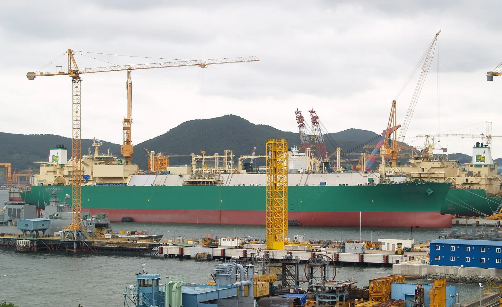 LNG carriers under construction at the DSME (now Hanwha Ocean) shipyard, with tower cranes and green hills behind.