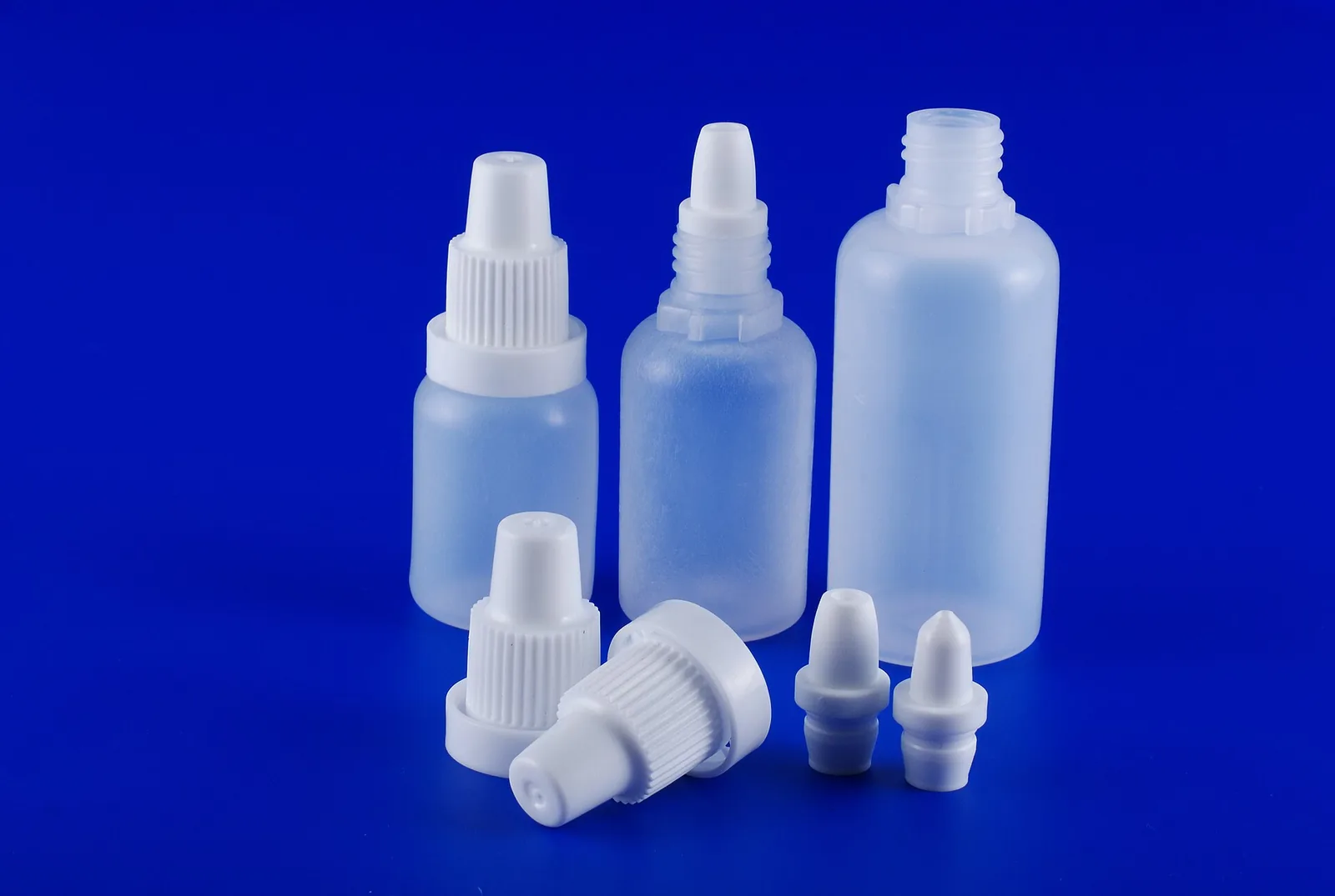 Empty plastic eye-drop dropper bottles in 10, 15 and 30 ml sizes with tamper-evident caps on a blue background.