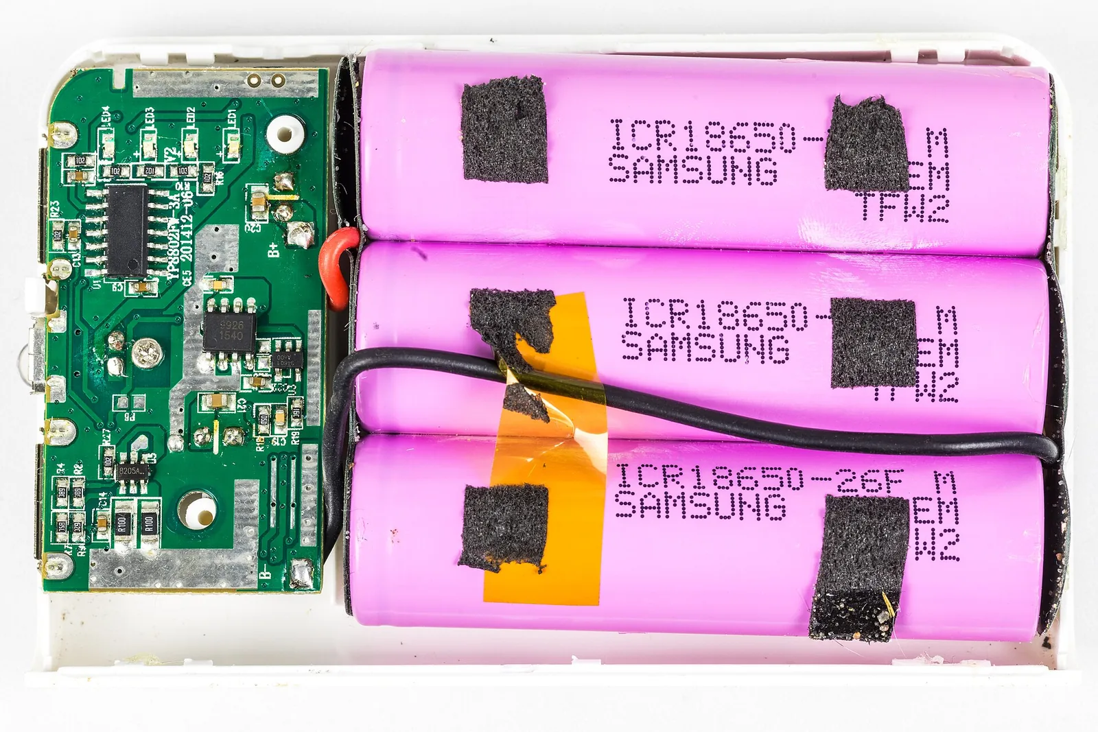 Three pink Samsung ICR18650-26F lithium-ion battery cells inside an opened power bank, next to its circuit board.